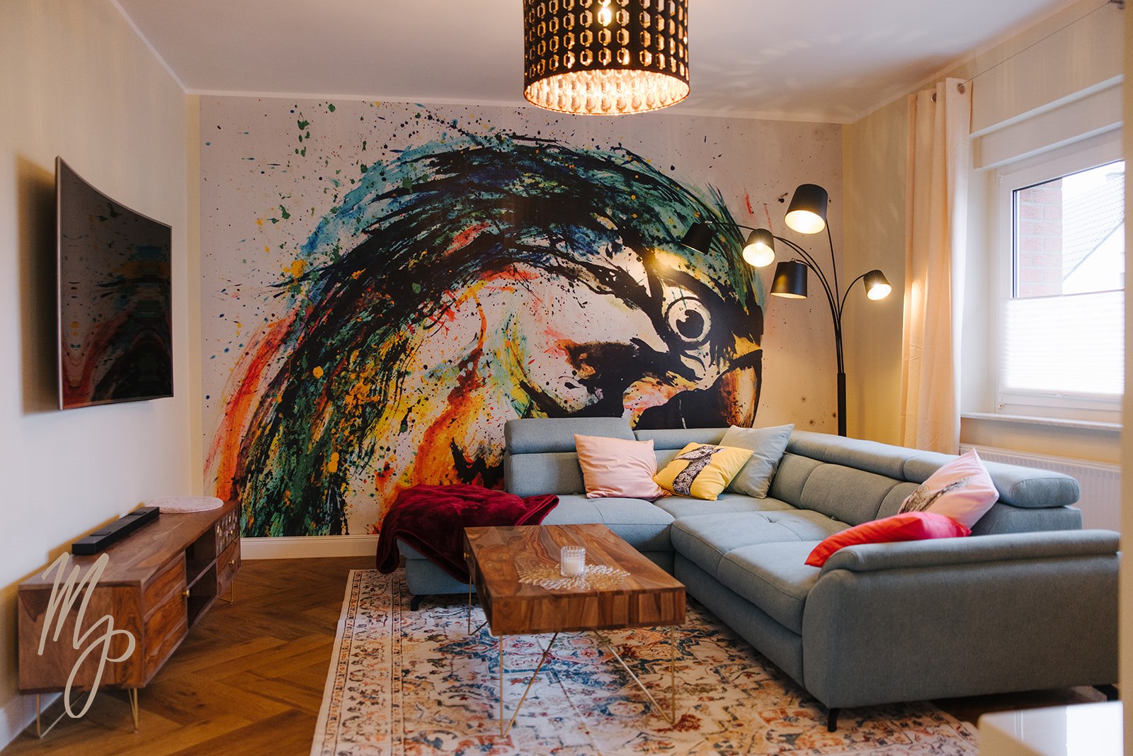 Wohnzimmer der Ferienwohnung mit farbenfrohem Papagei-Wandbild und gemütlicher Eckcouch